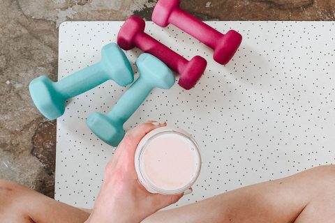 woman sitting on yoga mat with small weights and a smoothie in hand