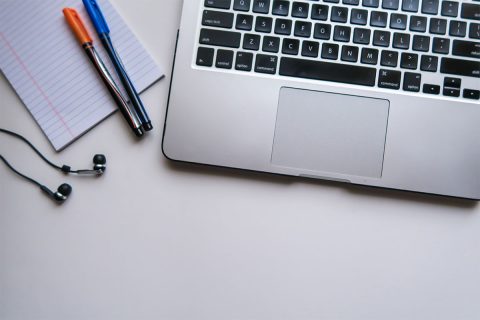 laptop next to pens a pad of paper and headphones