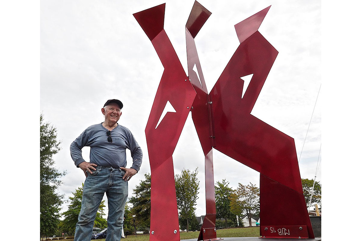 man next to red scultpure