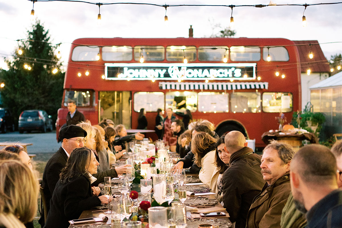 people dining at a large table outside of a double decker red bus