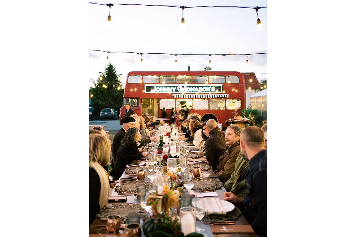 people dining at a large table outside of a double decker red bus