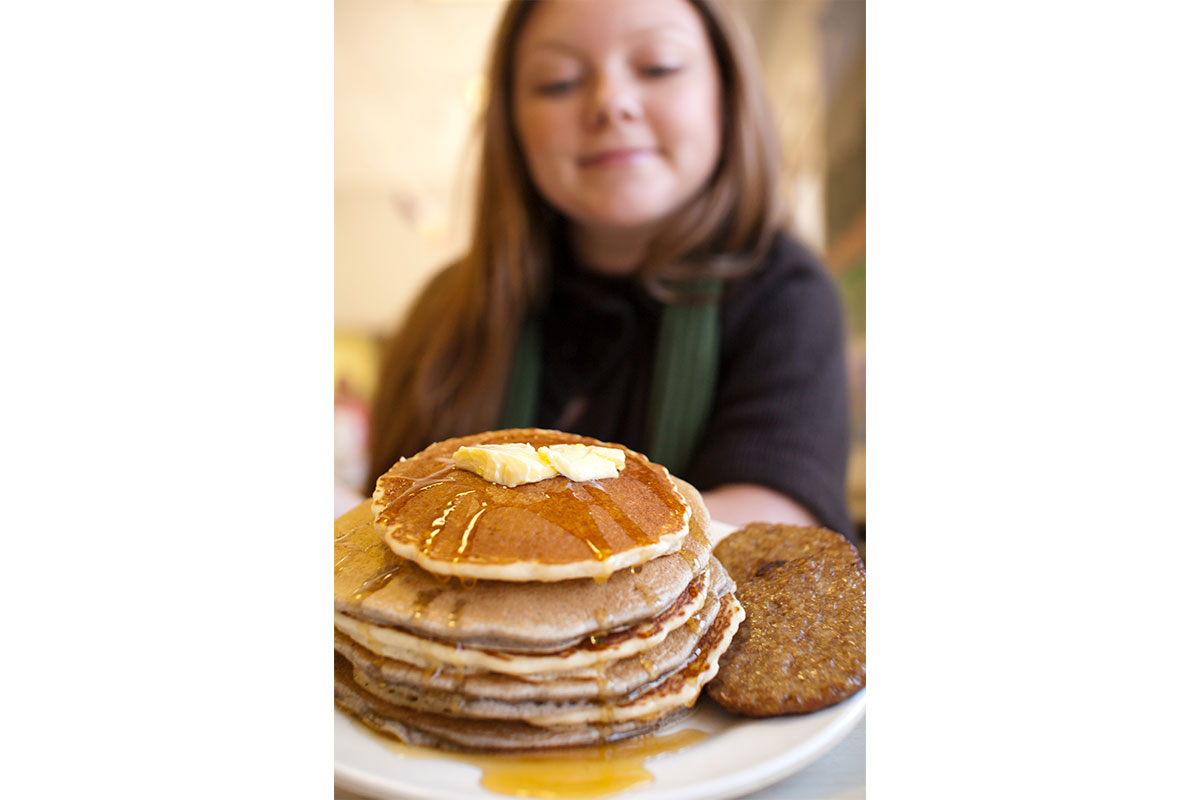 girl holding stack of pancakes with butter and syrup and sausage patties