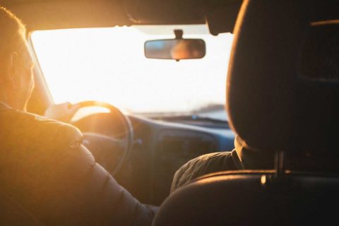 couple driving into sunlight in car with rearview mirror and black interior