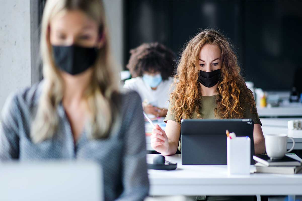 people working in office with black masks on and ipad