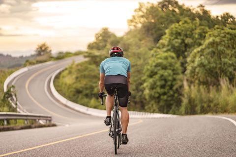 man biking down road with green trees