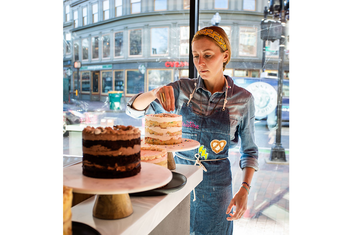 woman in overalls decorating a cake in front of a window