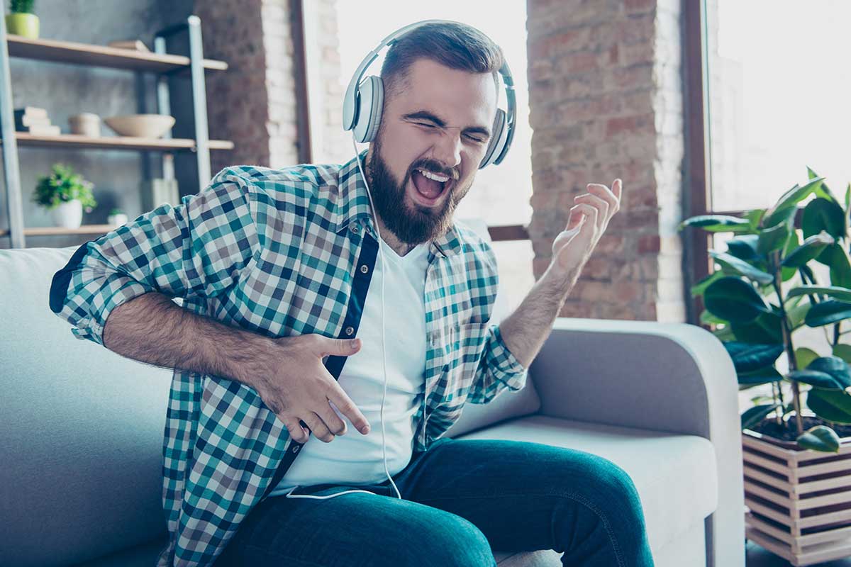man sitting on couch and listening to headphones while playing air guitar