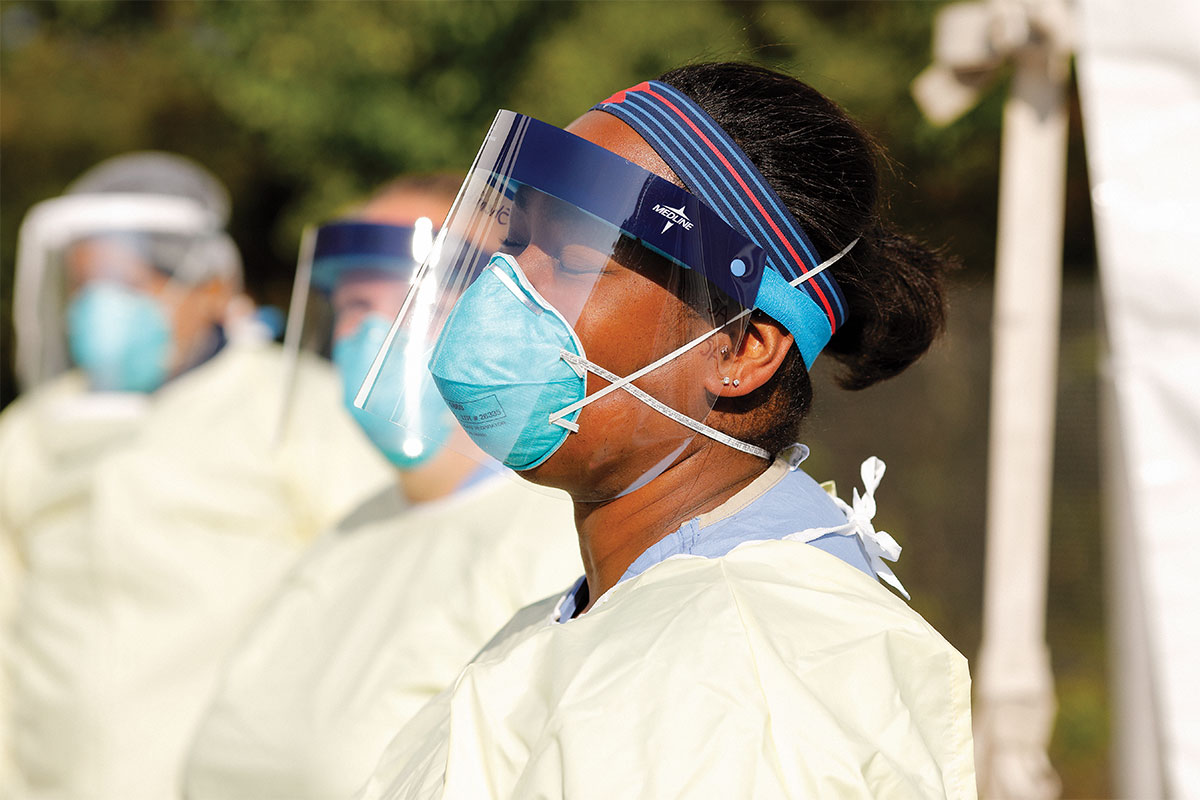 doctor standing outside in sun at covid-19 testing site with face shield mask and ppe