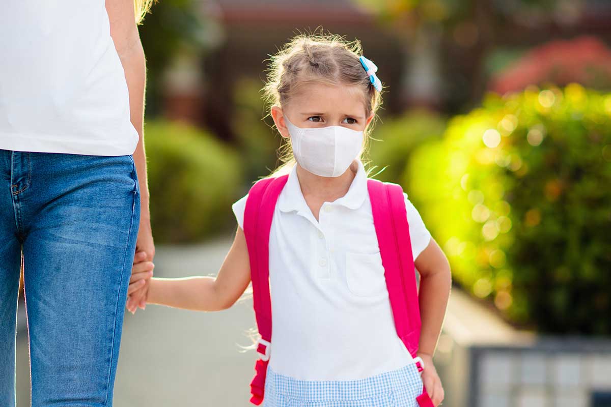 little girl holding hands with mom with white shirt and white mask and pink backpack