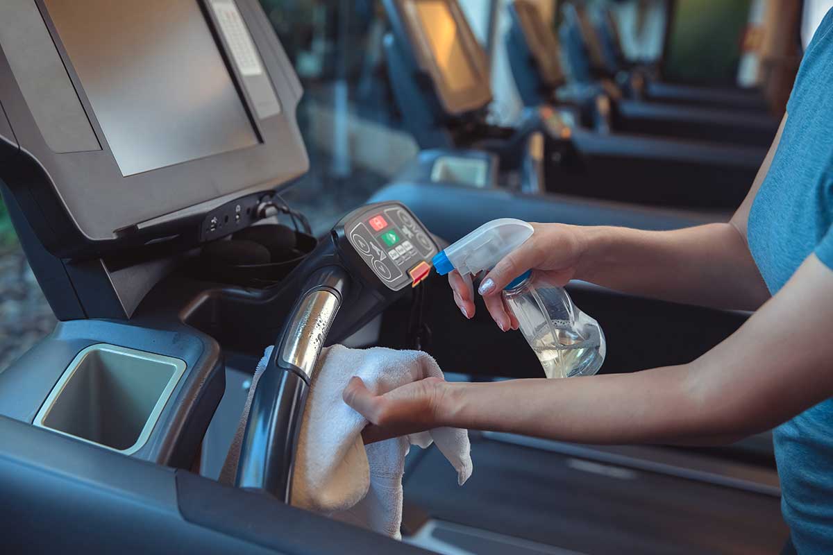 woman spraying down treadmill with spray bottle and towel