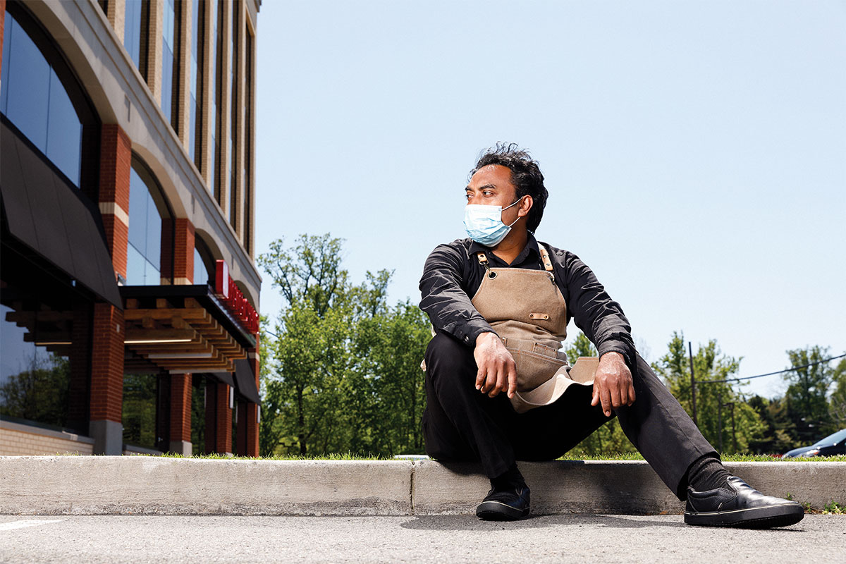 man sitting on curb wit mask outside of building