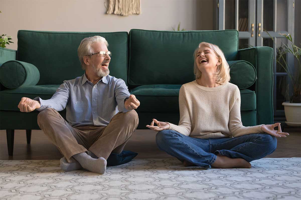senior man and woman sitting on floor laughing while meditating