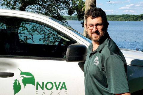 man in green polo standing next to water and nova parks truck
