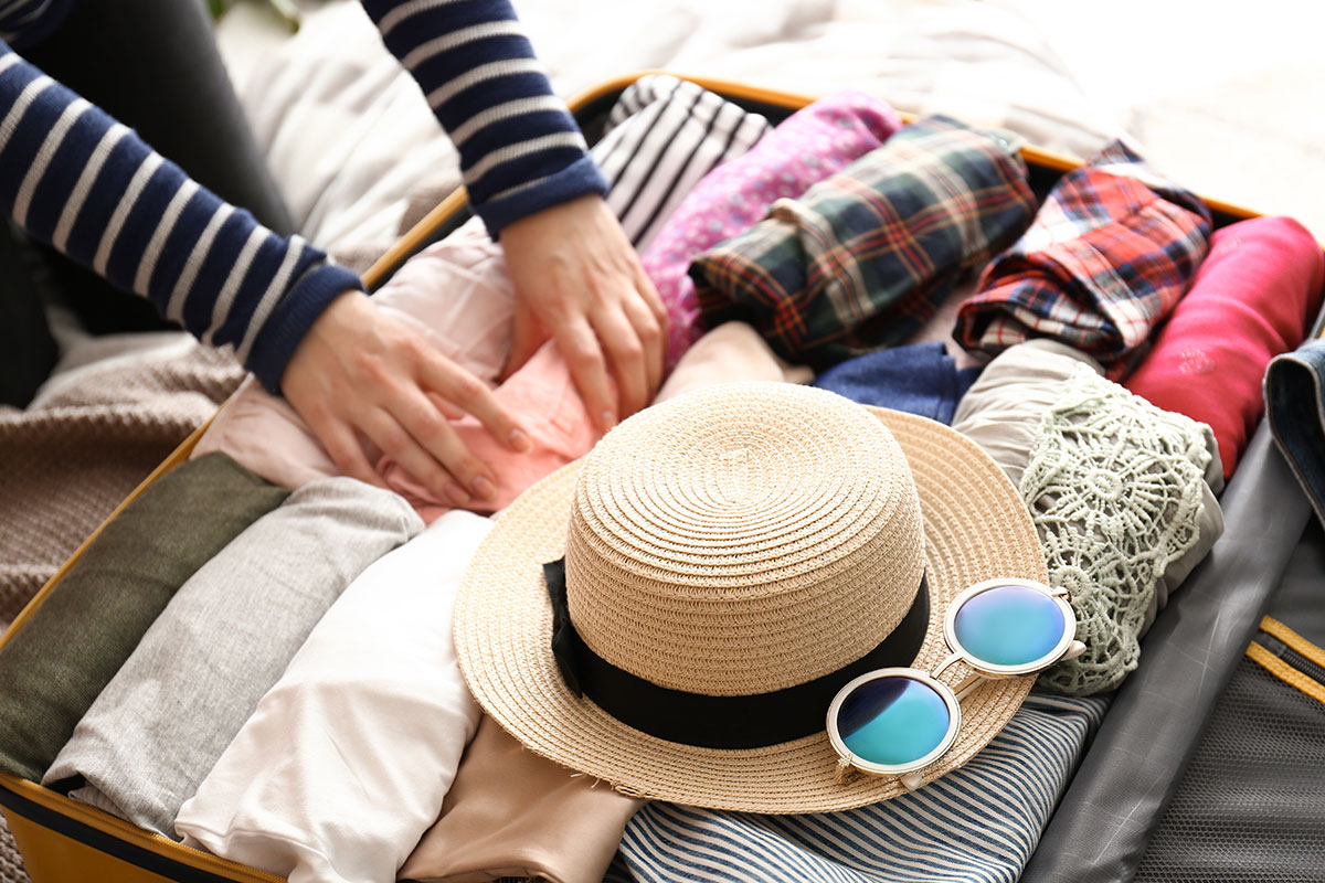 packing a suitcase with folded clothes and a straw hat with sunglasses