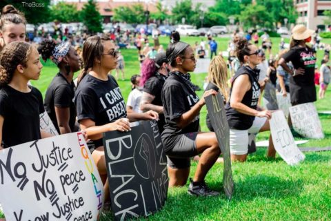 marchers kneeling in grass in manassas virginia with signs