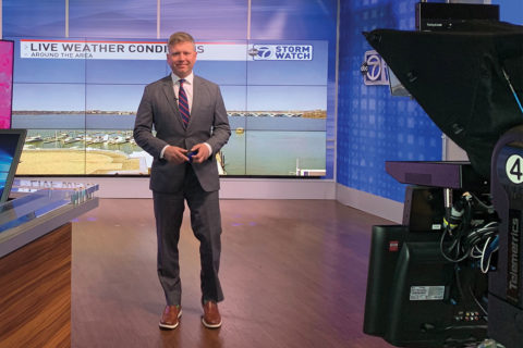 ryan miller standing in front of news screen with black camera
