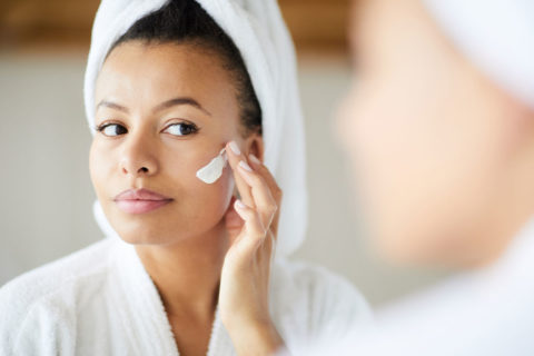 woman putting face cream on while in bathrobe
