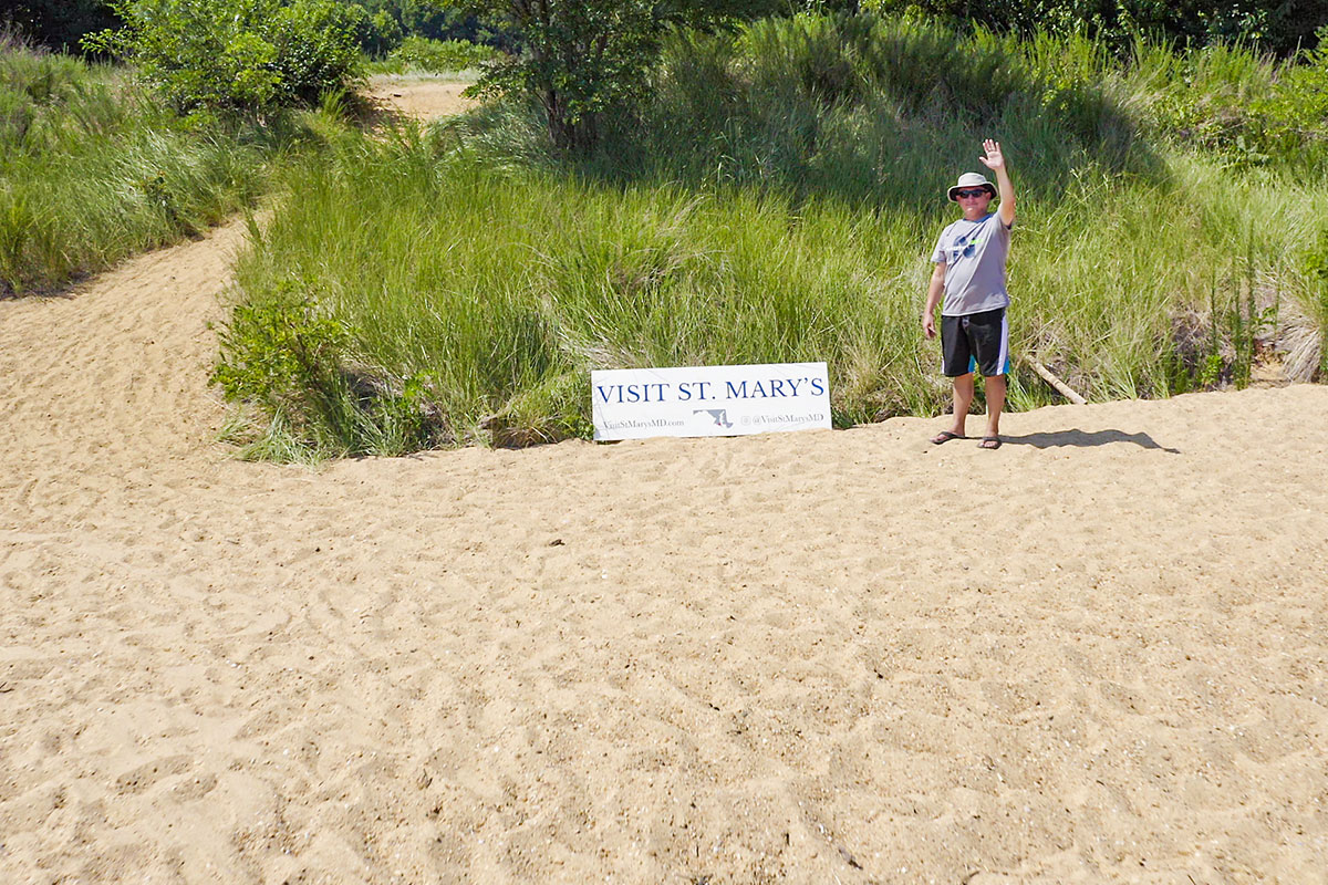 person waving on beach next to sign that says visit st. mary's county