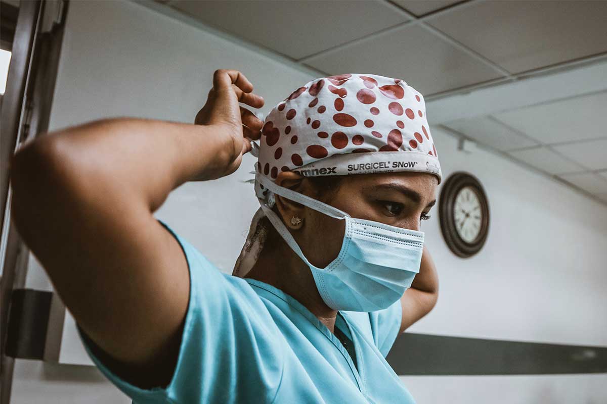 woman in scrubs tying up face mask