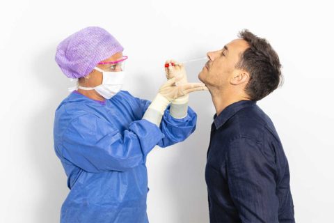 white man in blue shirt getting tested for covid-19 with nursge with ppe