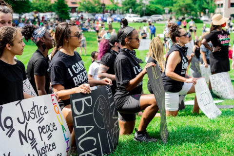 young women in field kneeling down with signs