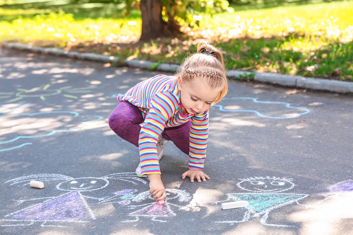 small girl drawing on concrete with chalk