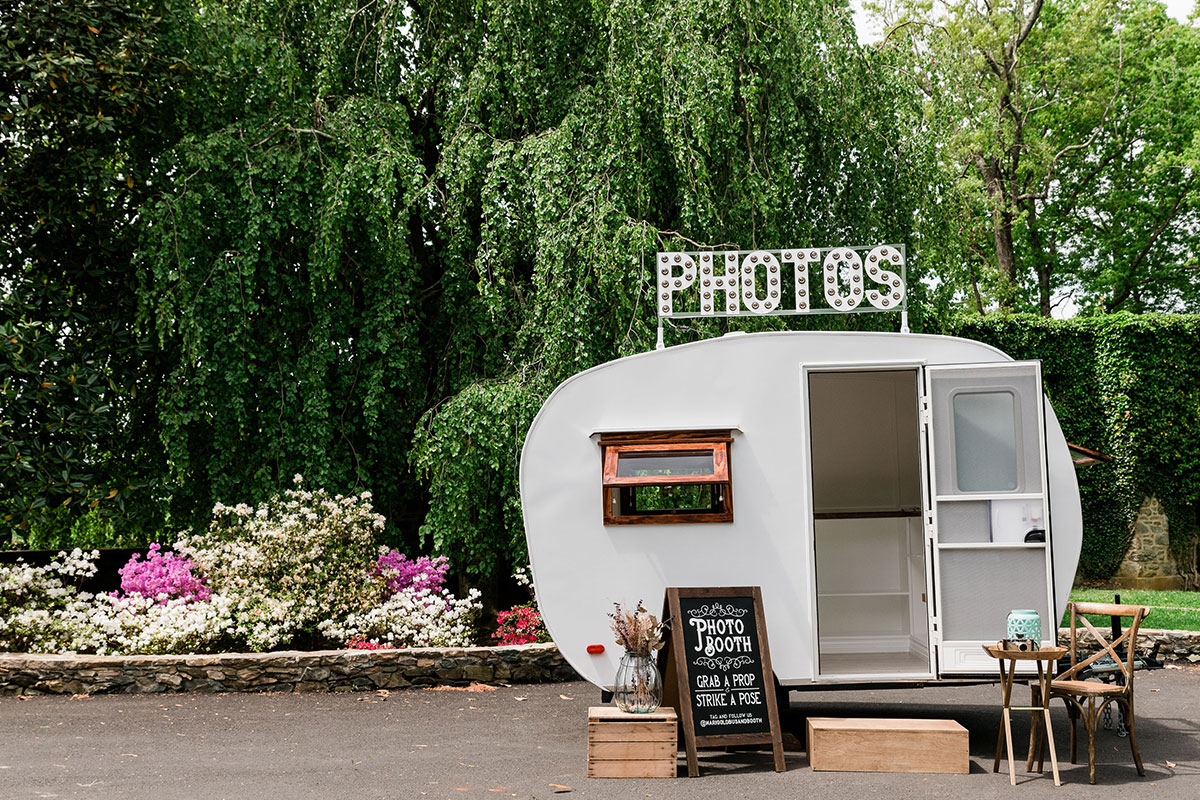 silver photo booth in front of willow trees