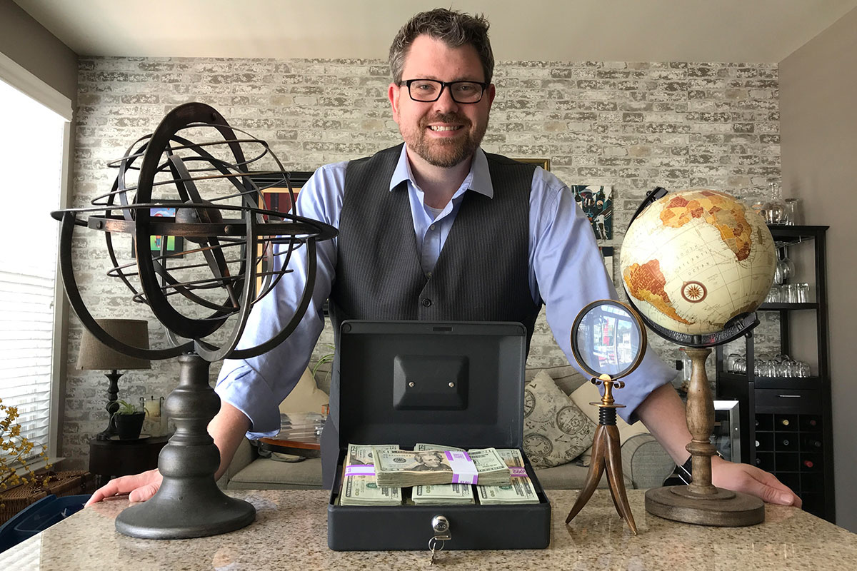 man standing next to a briefcase full of money and globes