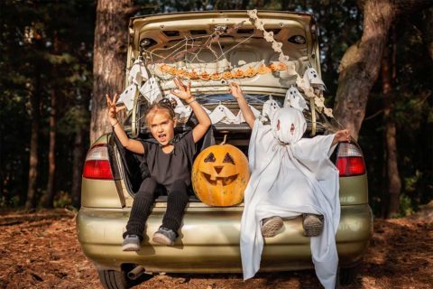 two kids sitting in trunk with Halloween decorations