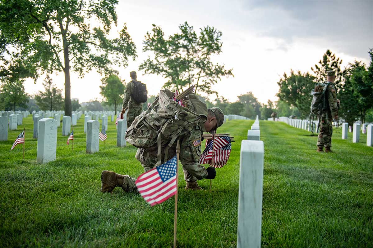 soldier putting flag in front of grave