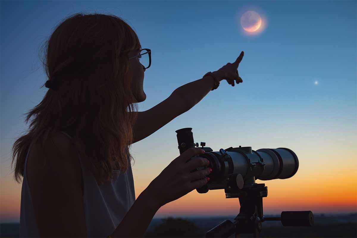 woman looking at night sky through telescope