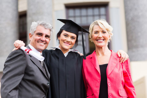 beautiful young female graduate with parents at ceremony