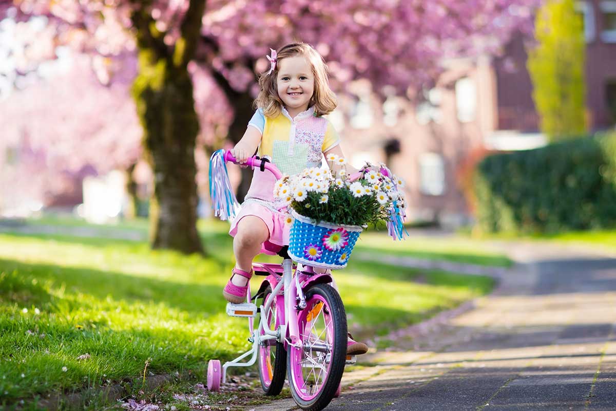 girl on pink bike with training wheels in front of cherry blossom tree