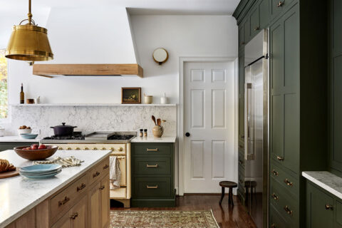A kitchen with light wood details on the island, light walls, and green cabinets