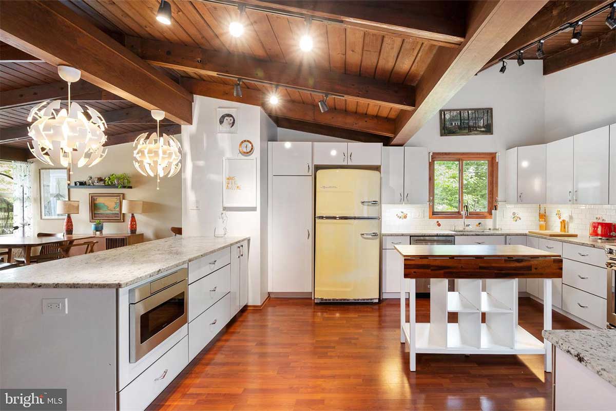 A kitchen with white cabinets and light granite countertops with a wood floor and ceiling.