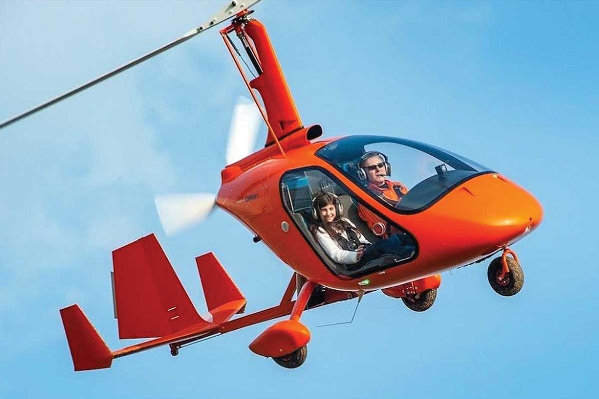 A man and girl fly in an orange ultralight aircraft, part of Flying Club 1. 