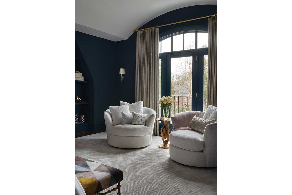 Two round arm chairs in front of a floor-to-ceiling window and a navy blue wall in bedroom.