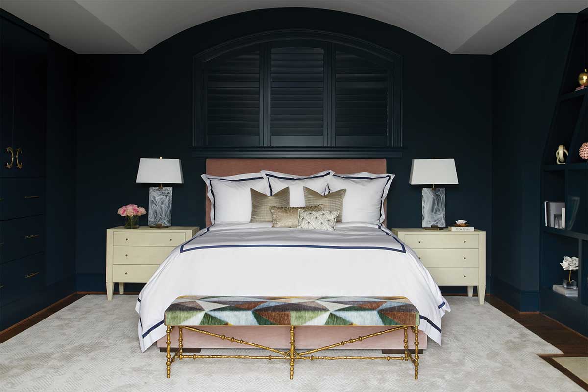 A navy blue room with a white bed in the center and white nightstand tables on either side in remodeled bedroom.