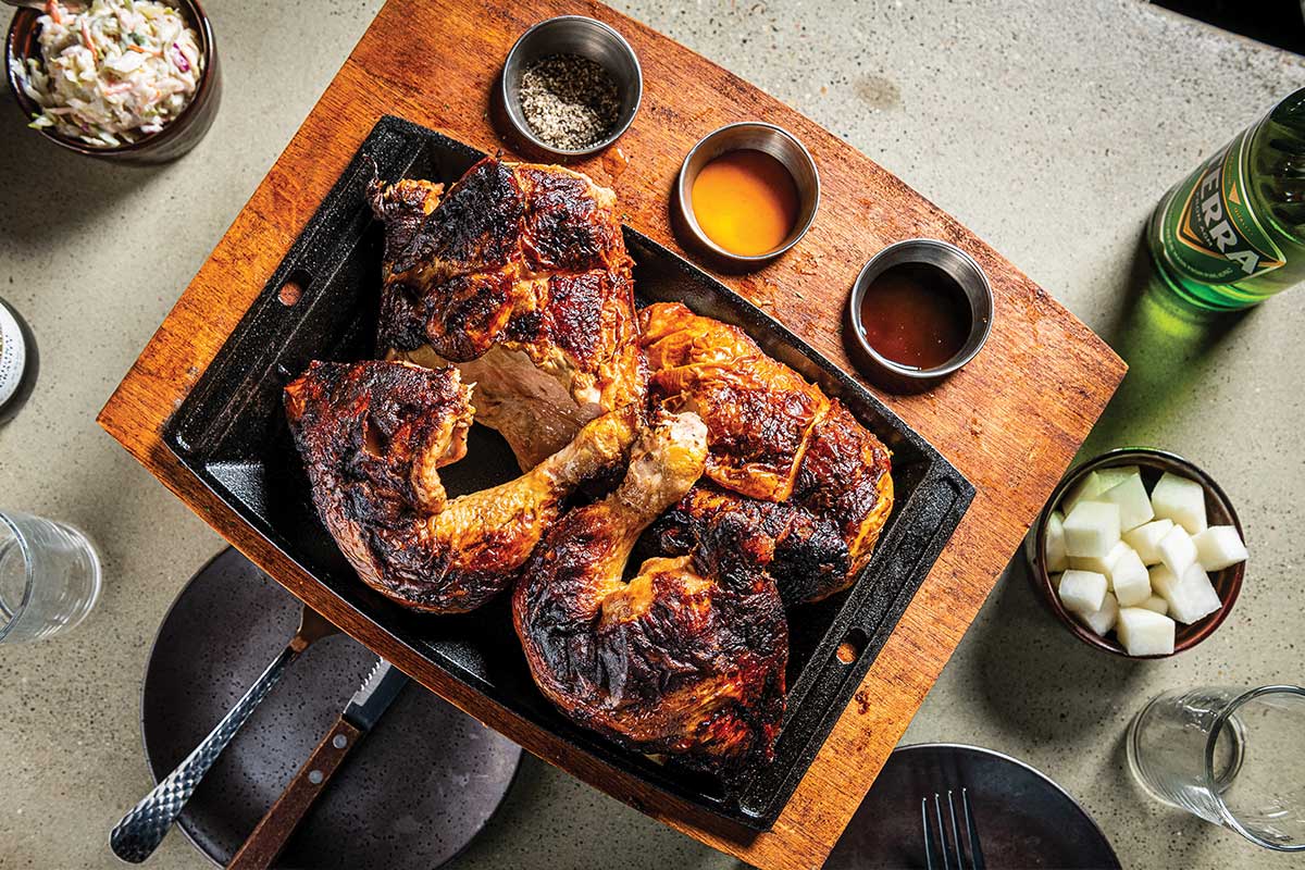 A wooden plate with chicken and three sauces.