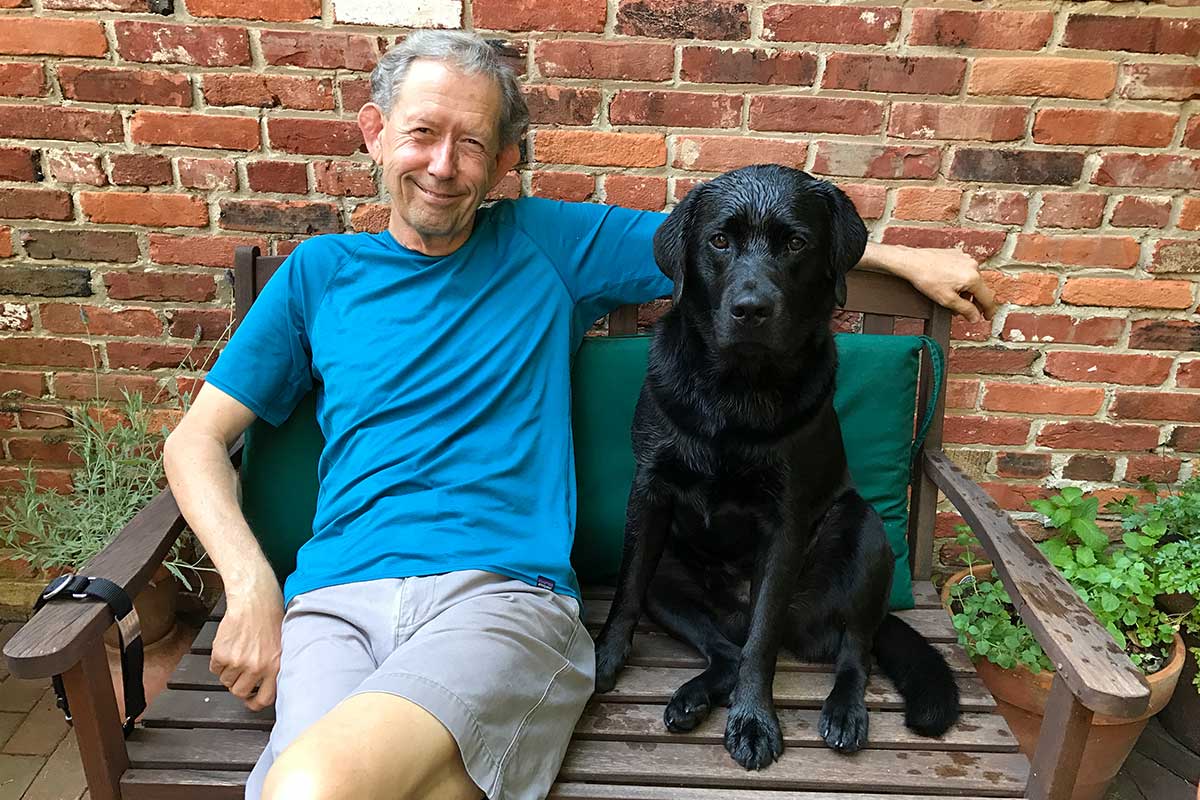 Mitchell sitting on a wooden bench next to his black dog Andre. 