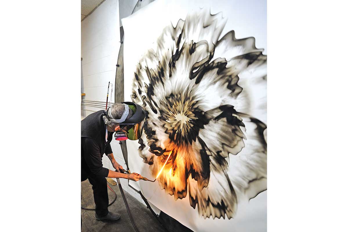 Mitchell uses a blowtorch to make a large black and white piece of artwork. 