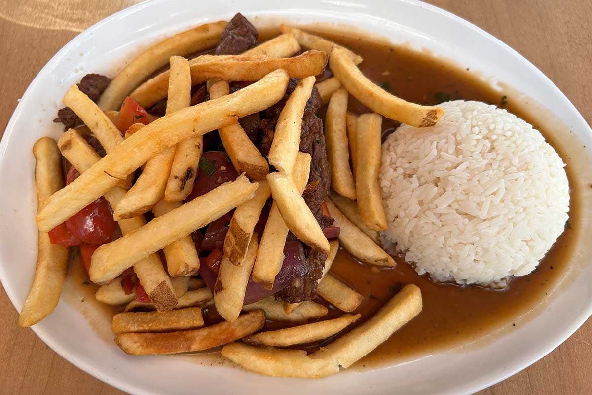 white rice with fries covering tenderloin, onions, and tomatoes
