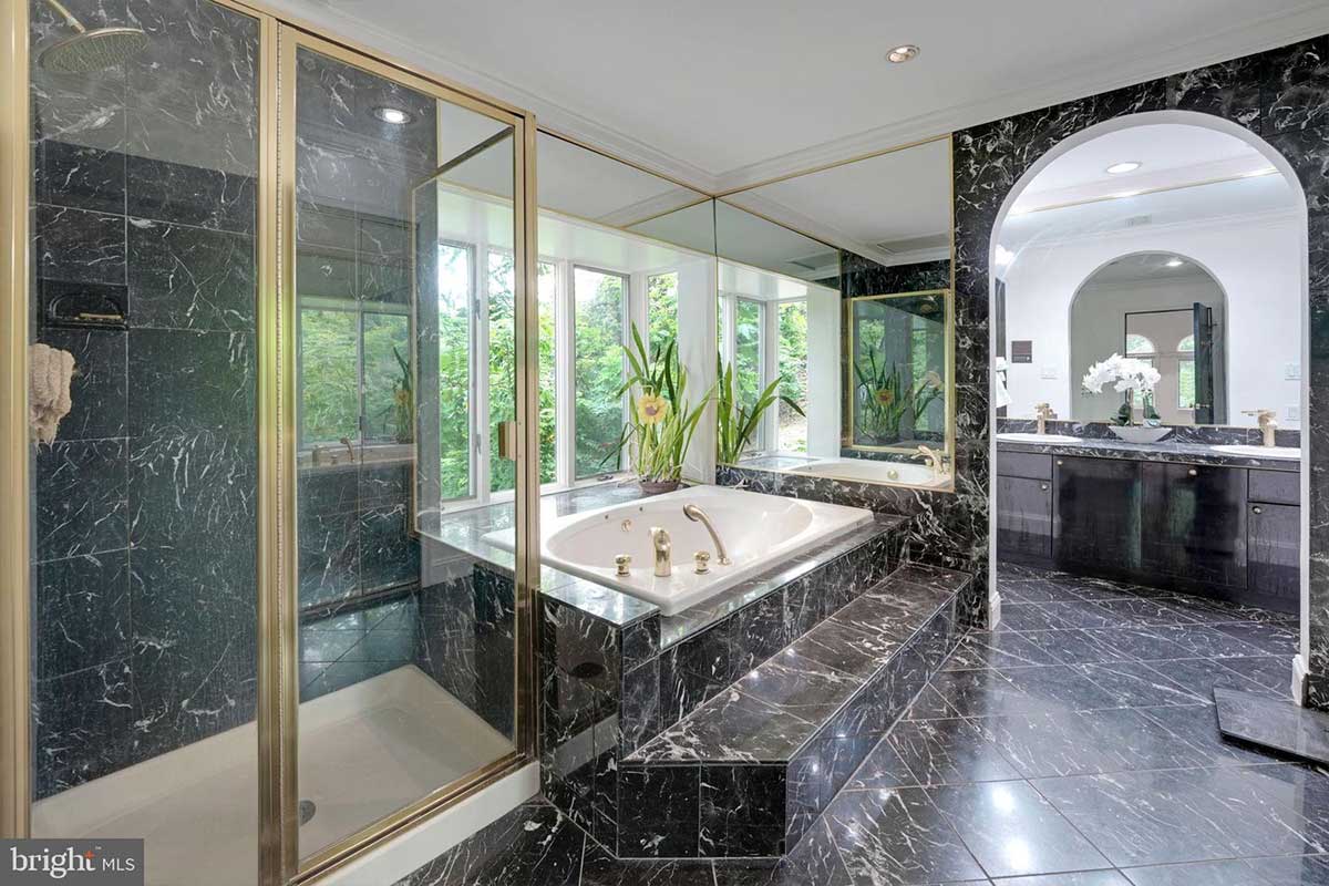 bathroom covered in black marble tiles with soaking tub and walk-in shower