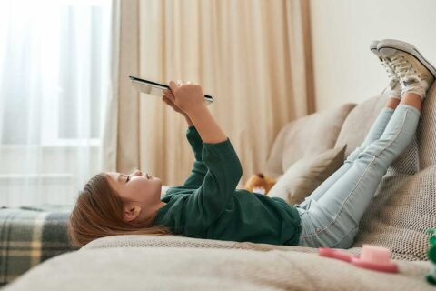 child laying on couch looking at tablet
