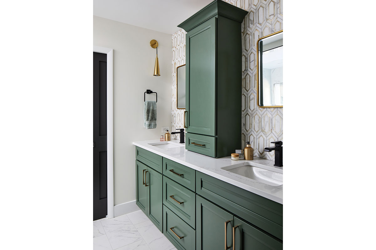 Bathroom vanity with green cabinets, marble counter, and white and gold geometric backsplash