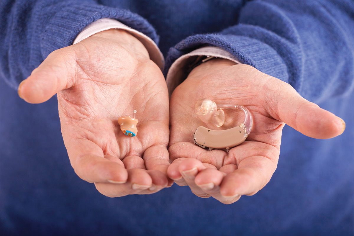 Person holding two different models of hearing aids