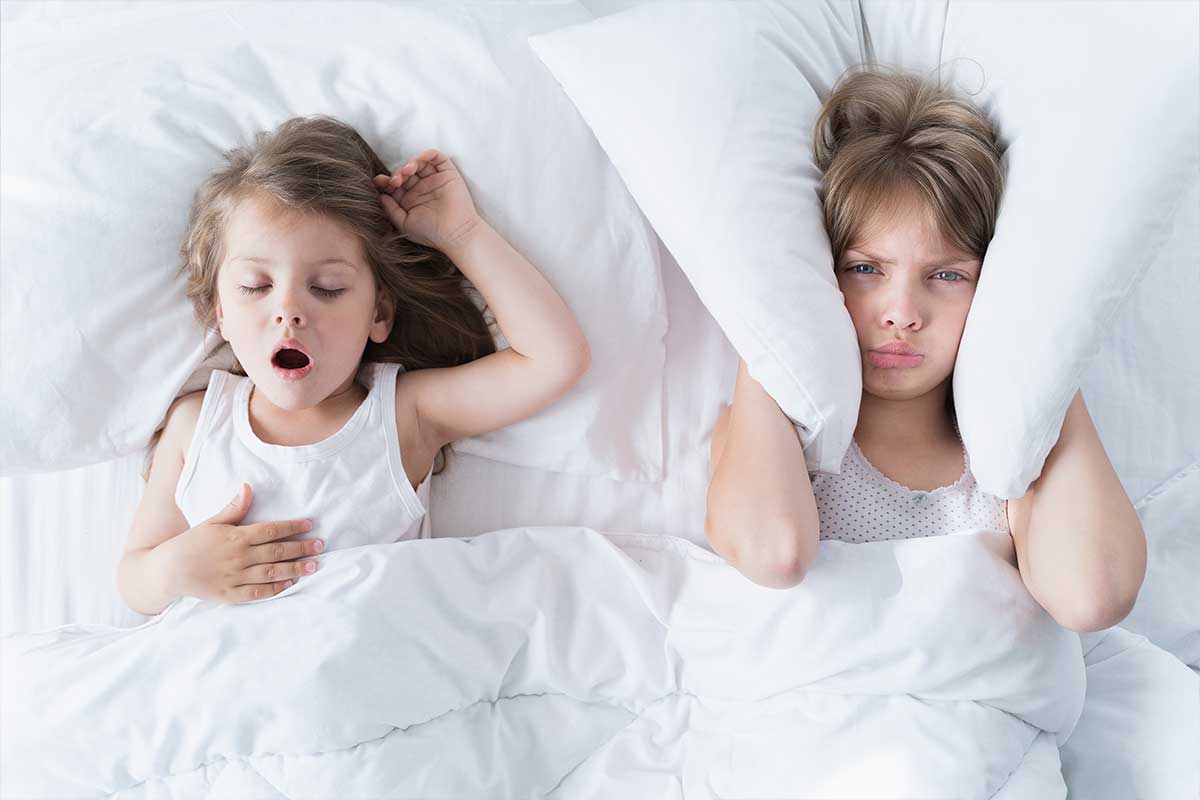 child with pillow over ears while other child sleeps
