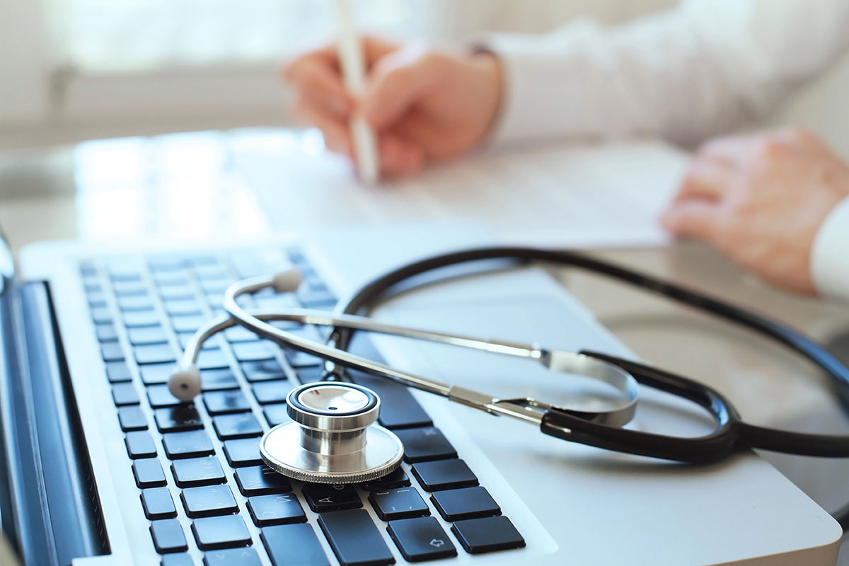 computer with stethoscope on it and doctor in background