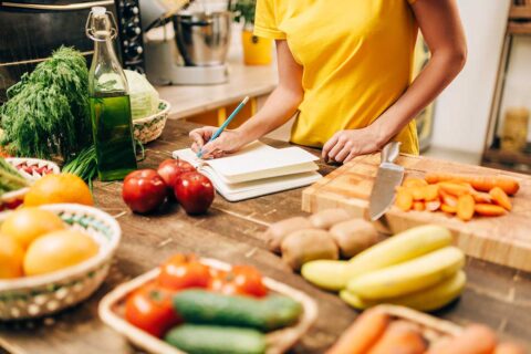 person cooking with fresh vegetables, taking notes