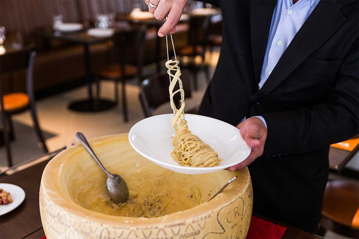 server with plate of pasta and cheese wheel